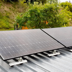 Dach mit zwei Solarpanelen, umgeben von Bäumen und Grünflächen.