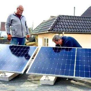 Zwei Männer installieren Solarpanels auf einem Dach.